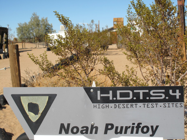 A photograph of a sign reading "High. Desert. Test. Sites." and "Noah Purifoy"