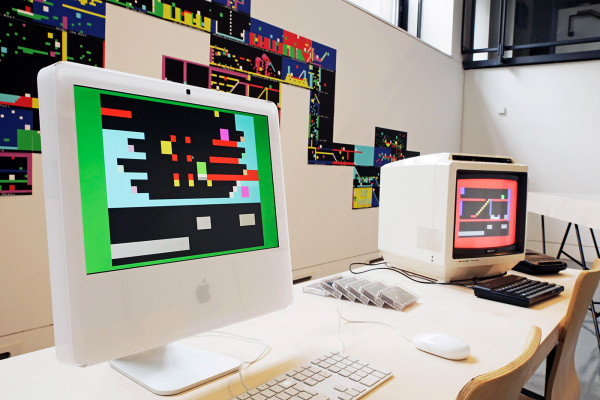 A photograph of two computer screens displaying artwork by JODI