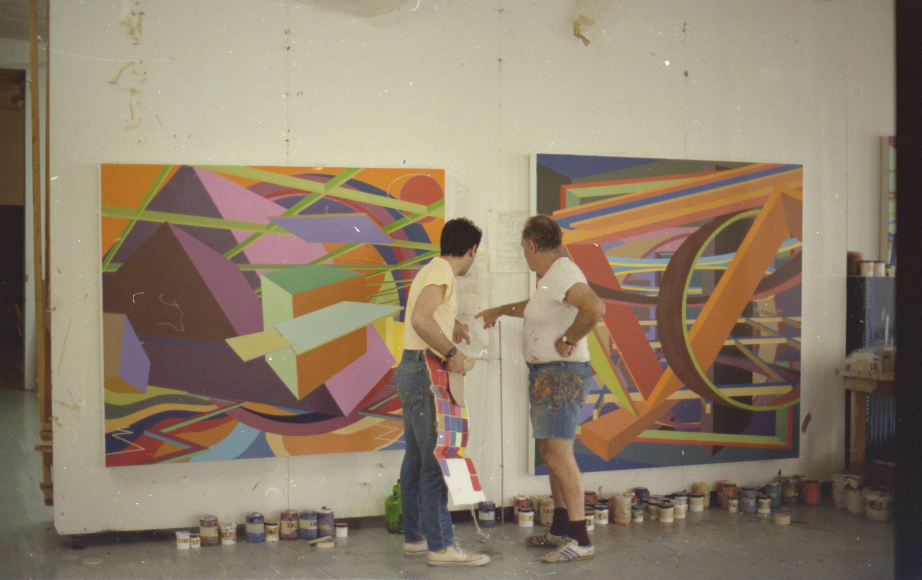 Two men having a conversation in the middle of two large abstract paintings.