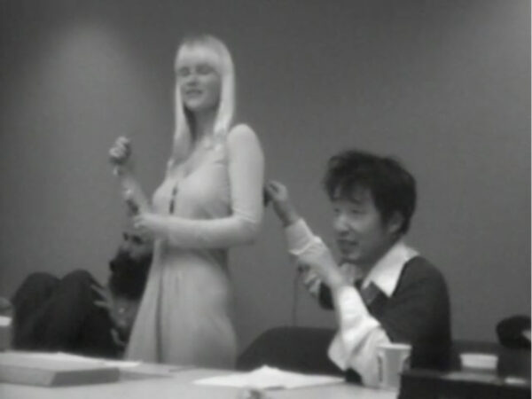 black-and-white screenshot showing a woman modeling a dress next to a man.