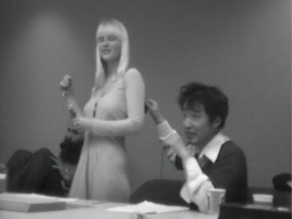 lack-and-white screenshot showing a woman modeling a dress next to a man. 