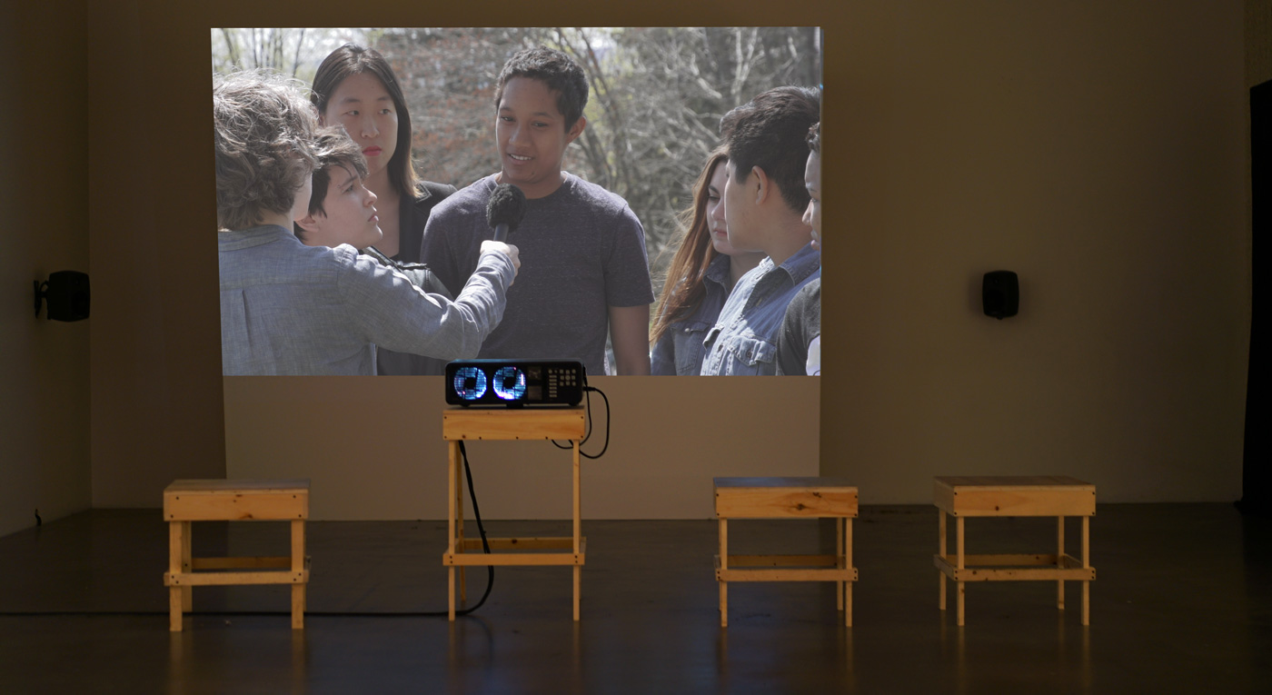 photo of a video art installation showing a group of young people being interviewed 