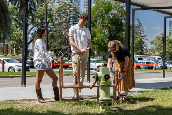 Three people stand around a drinking fountain