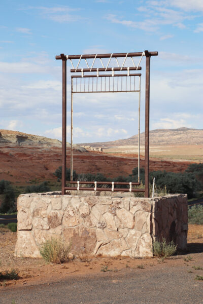 A rectangular metal frame stands vertically atop a four-walled stone base in a desert landscape