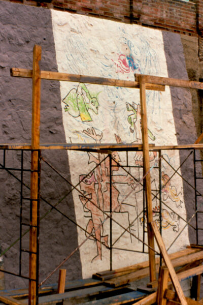 An outdoor mural on a wall with a scaffolding in front of it