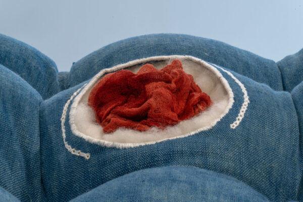 A close-up of a textile artwork featuring blue and orange fabric, stuffing, and white thread